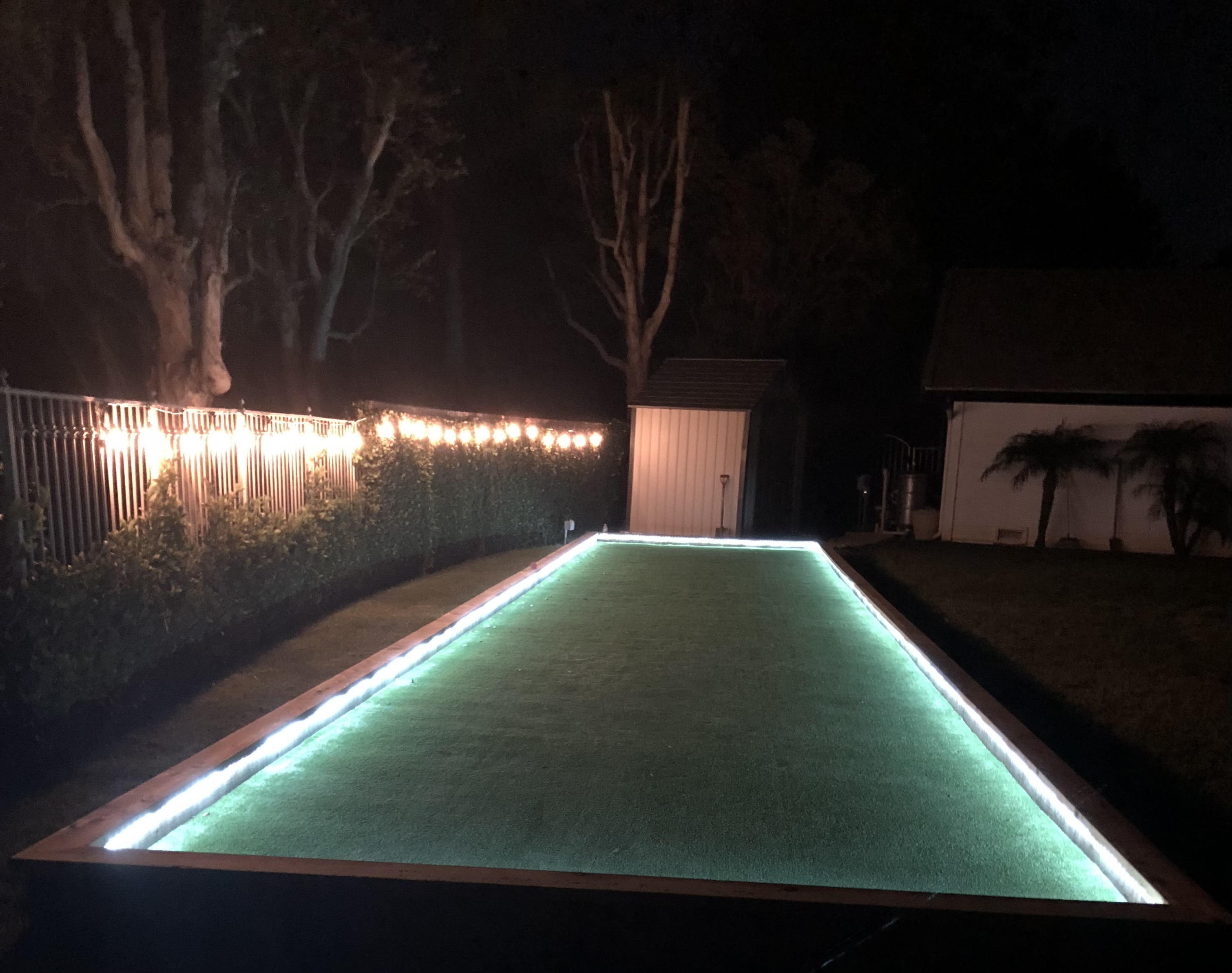 Backyard bocce ball court on artificial turf with LED accent lighting at night - Green Forever Turf Texas